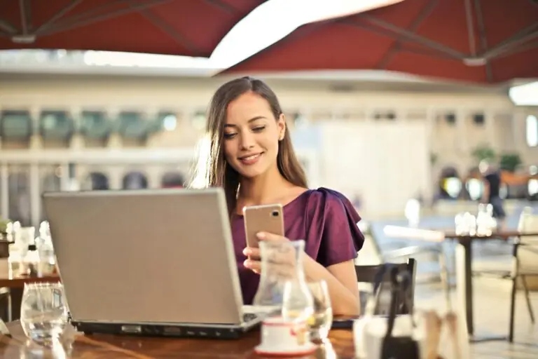 A young professional woman working on a computer laptop while checking her smartphone, representing the Promolyday smart modern living niche.